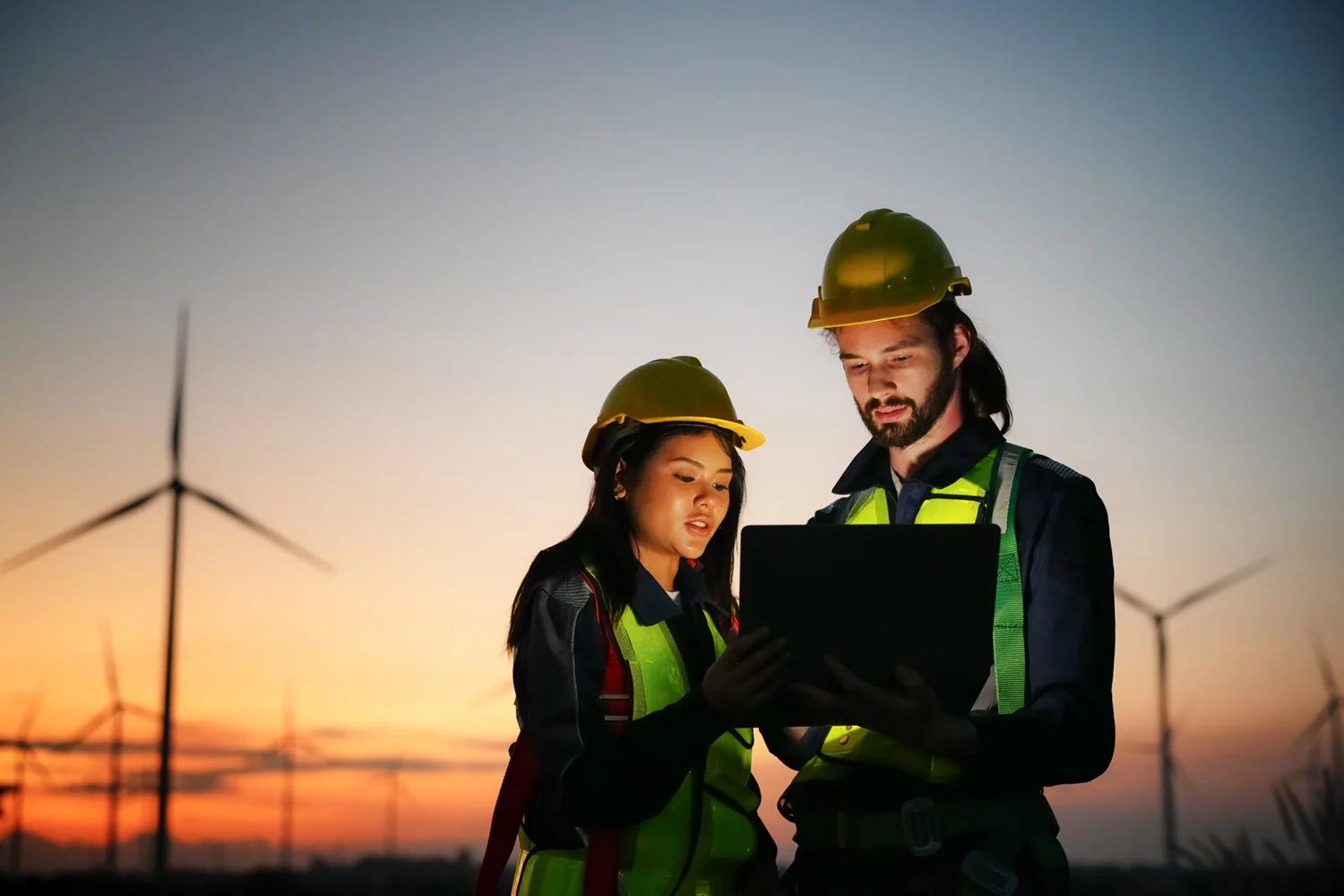 colleagues examining wind turbines at dusk